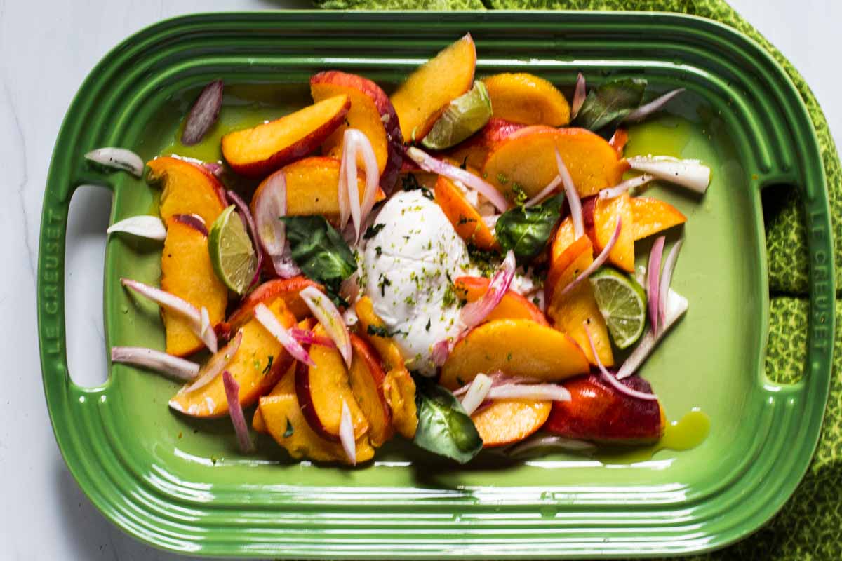 Peach Burrata Salad with fresh basil served on a le creuset serving platter. 