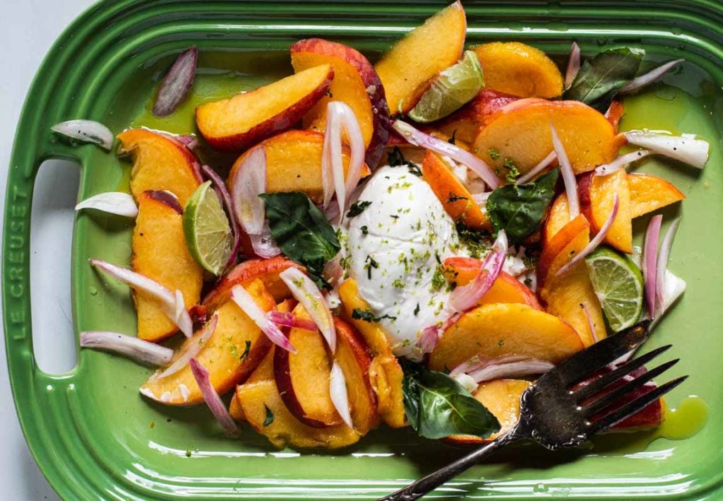 Peach salad recipe with burrata cheese and fresh basil on a le creuset green platter.