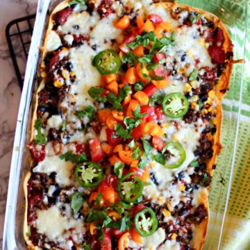 Layered Mexican Casserole in a 9 x 13 pyrex dish with ground beef and corn tortillas, garnished with tomatoes and cilantro