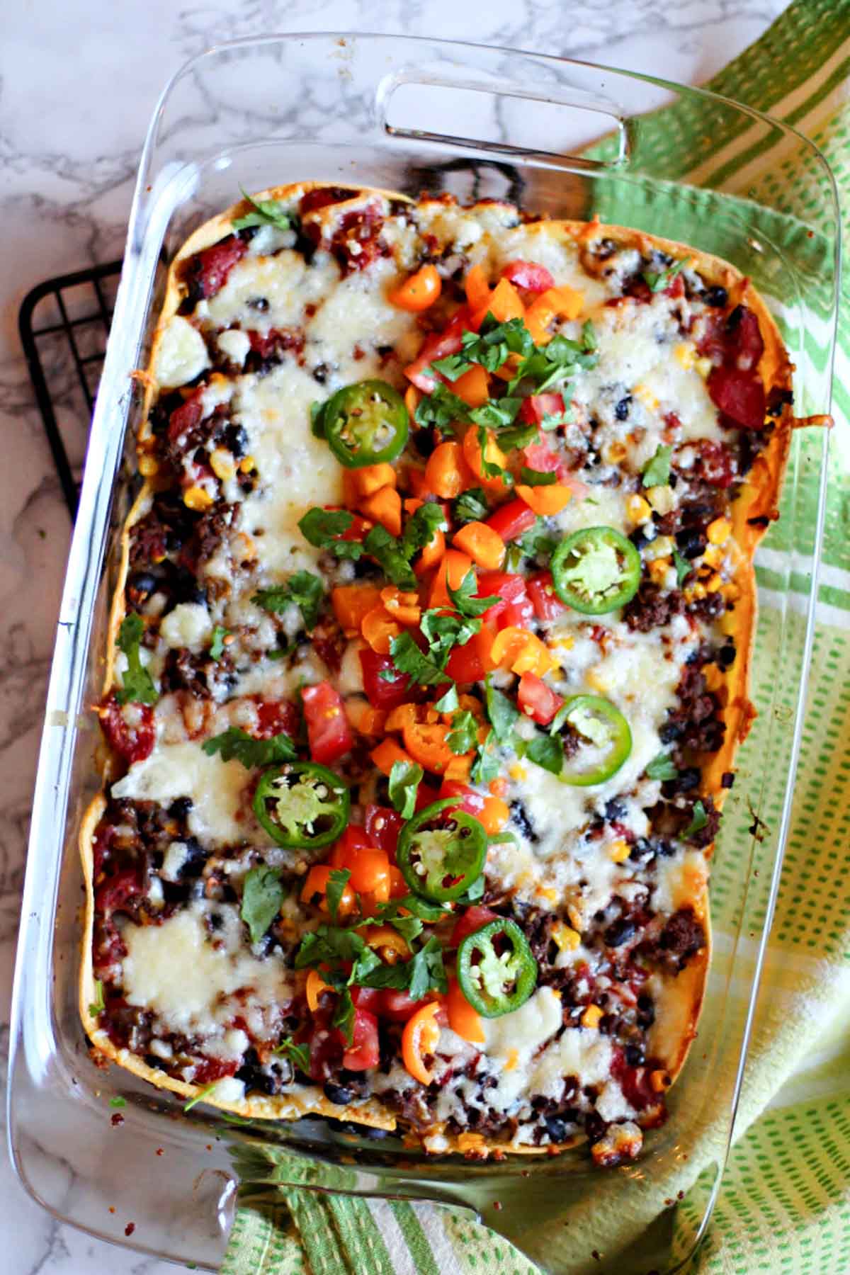 Layered Mexican Casserole in a 9 x 13 pyrex dish with ground beef and corn tortillas, garnished with tomatoes and cilantro