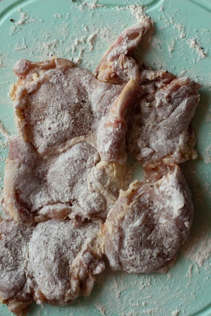 Dusting boneless skinless chicken breasts with flour.