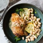 Pan fried chicken thighs on a dark blue plate served with beans and lemon cream sauce.