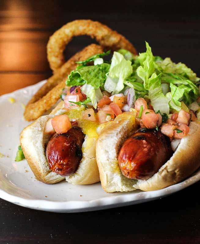 Two taco hot dogs on a white plate.
