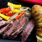 Bison New York Strip steak with red and yellow bell peppers and a sliced baked potato