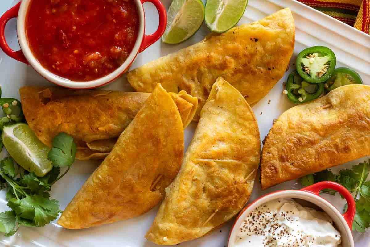 A platter of fried tacos served with sour cream and salsa.