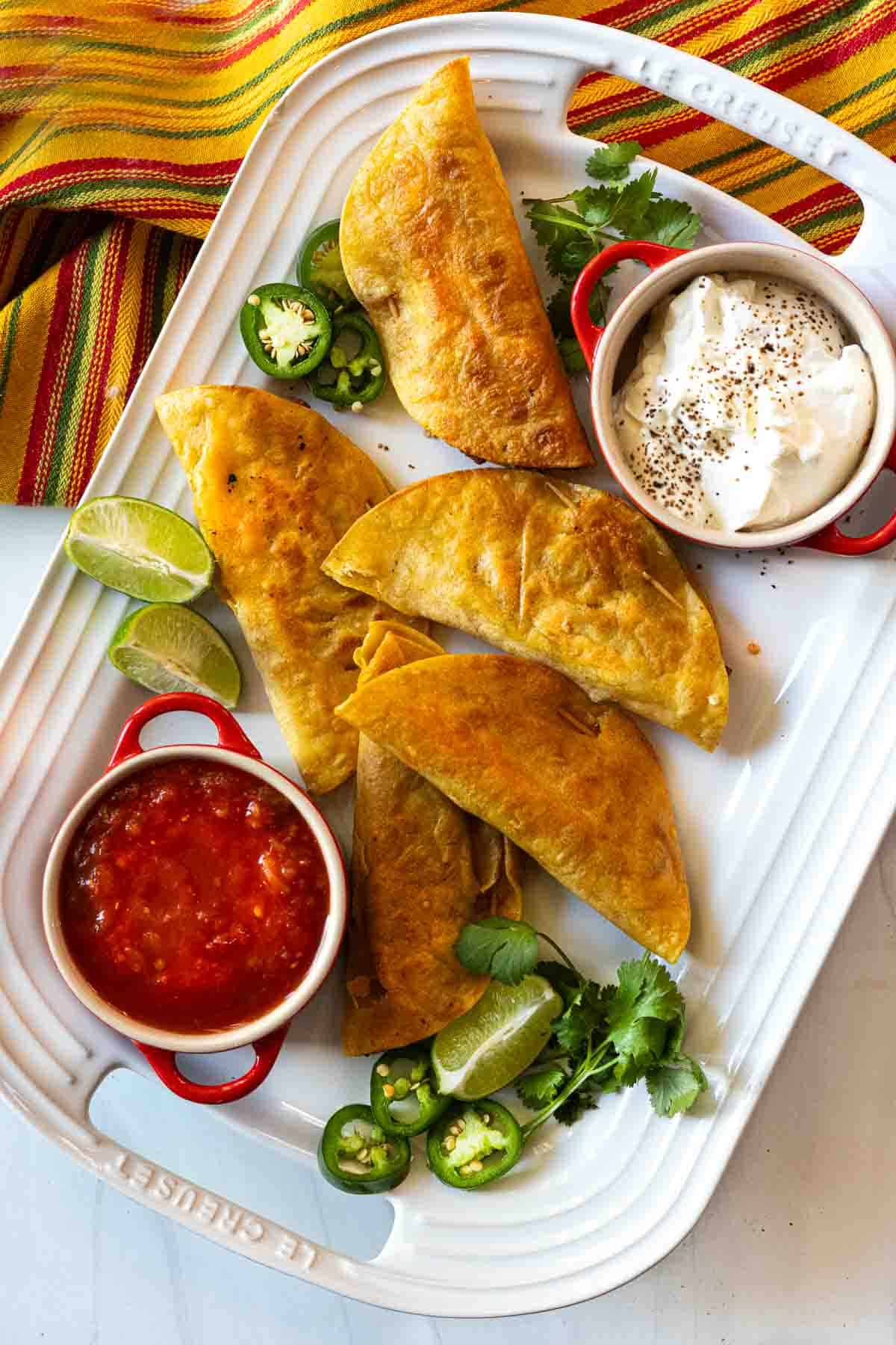 Authentic Mexican Fried Tacos on a white platter served with salsa and sour cream.