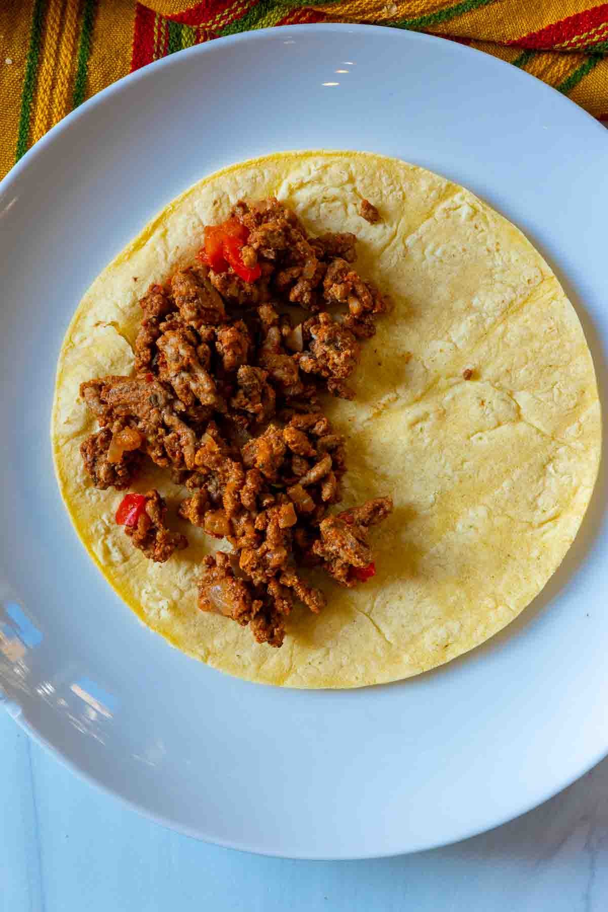 Adding seasoned meat to a corn tortilla to make fried tacos.