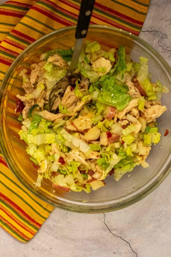 Adding romaine lettuce to ingredients to make chicken salad tacos.