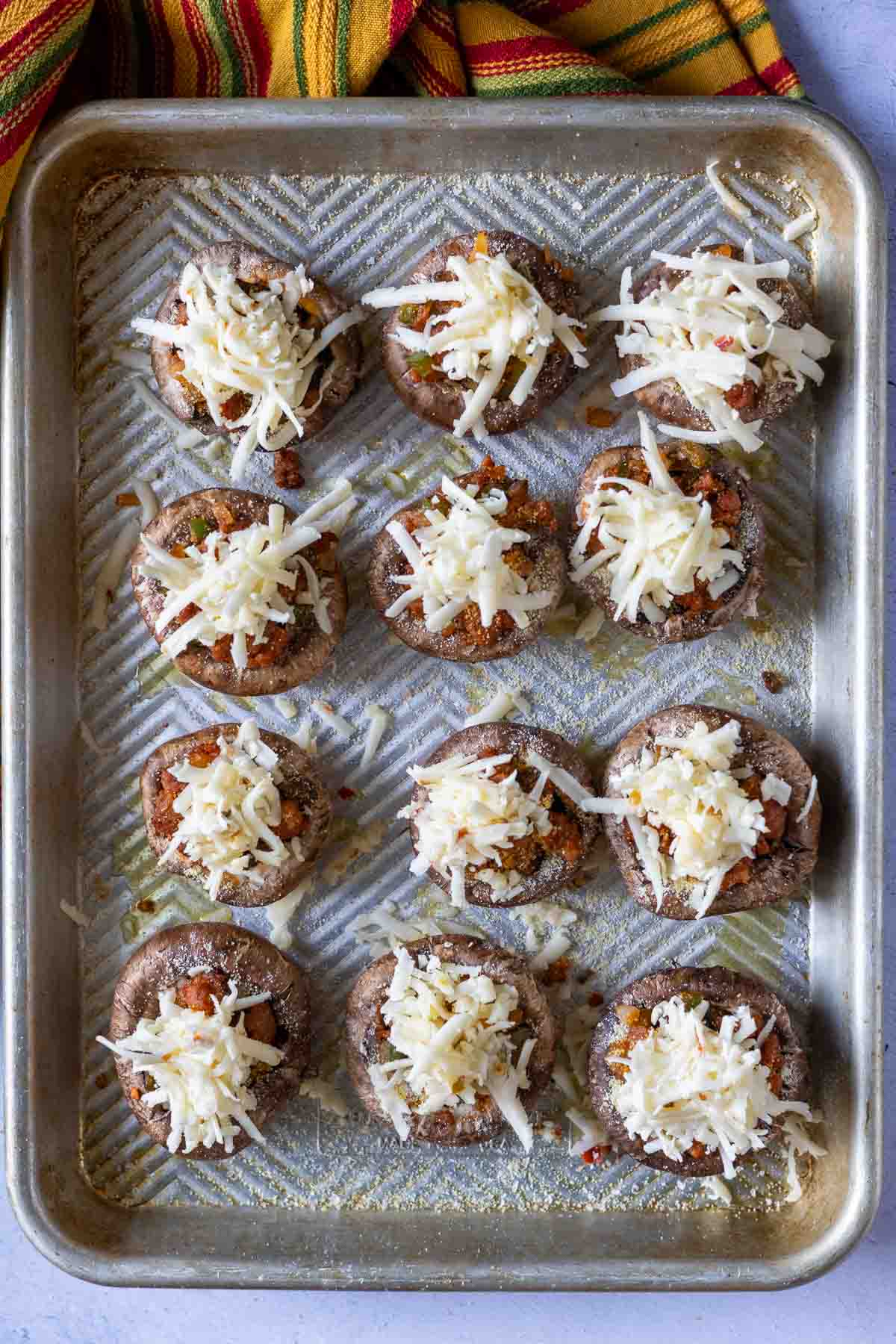 Chorizo stuffed muchrooms on a baking sheet with shredded cheese topping.