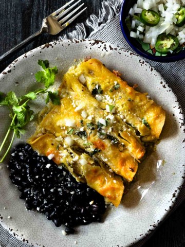 Pulled pork enchiladas verde served on a rustic plate with black beans.