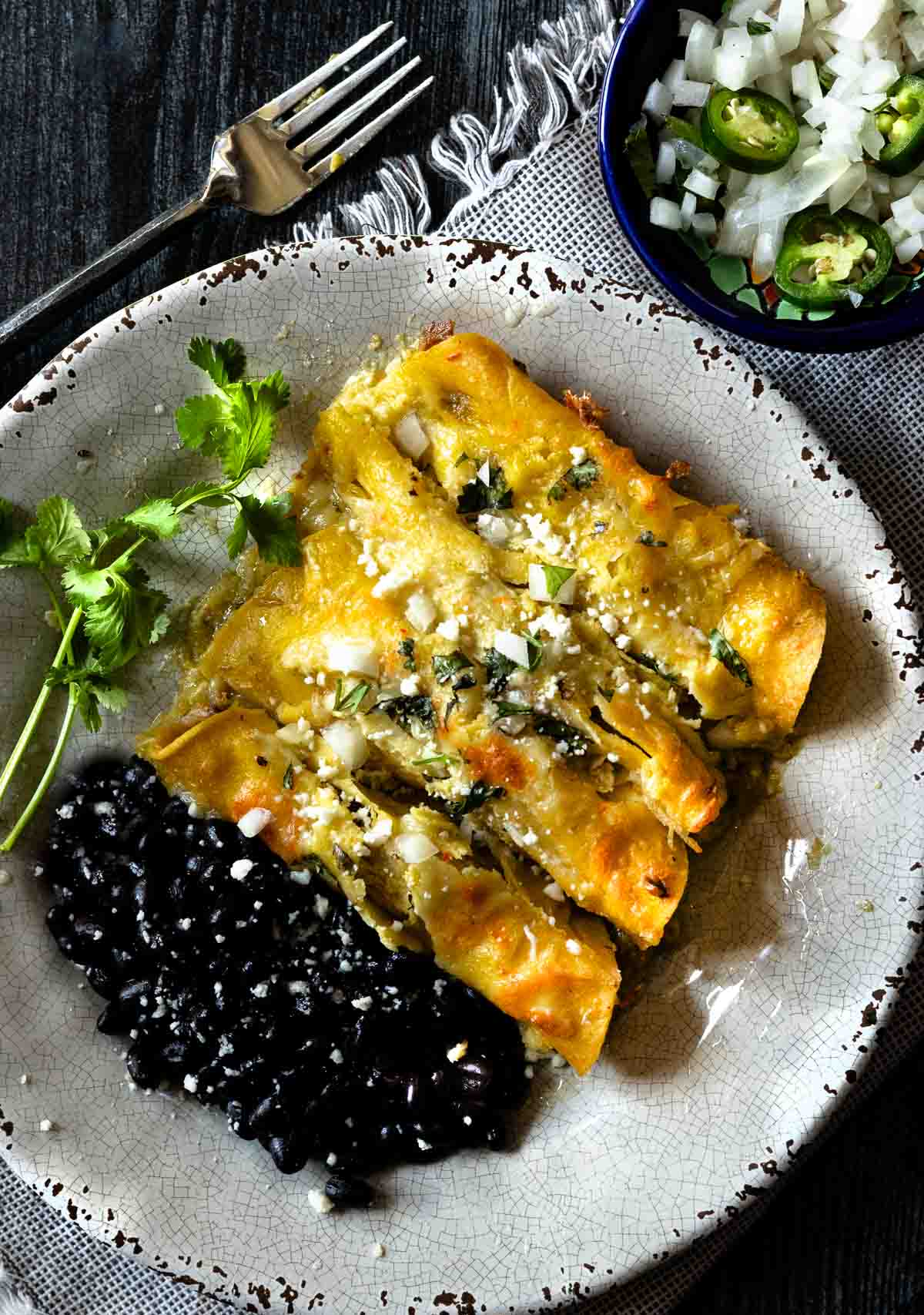 Pulled pork enchiladas verde served on a rustic plate with black beans.