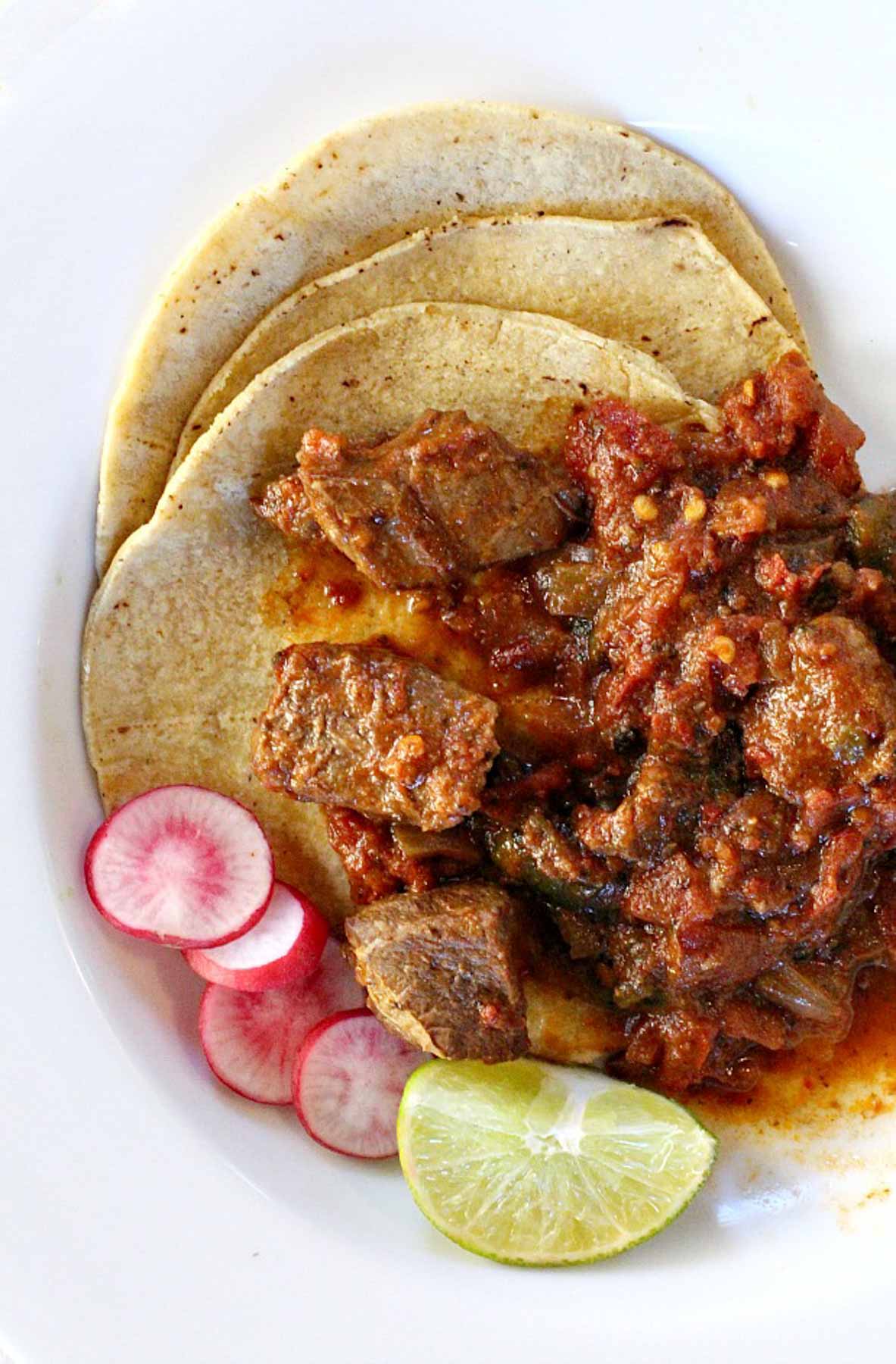 Mexican pot roast on corn tortillas garnished with radishes and limes.