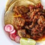 Mexican pot roast served over corn tortillas and garnished with sliced radishes and a wedge of lime.
