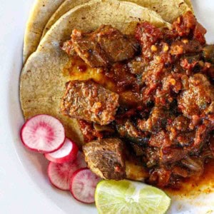 Mexican pot roast served over corn tortillas and garnished with sliced radishes and a wedge of lime.