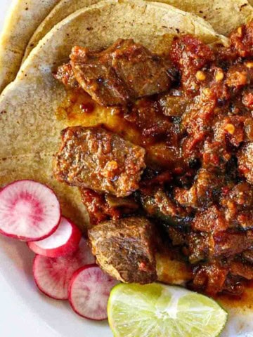 Mexican pot roast served over corn tortillas and garnished with sliced radishes and a wedge of lime.