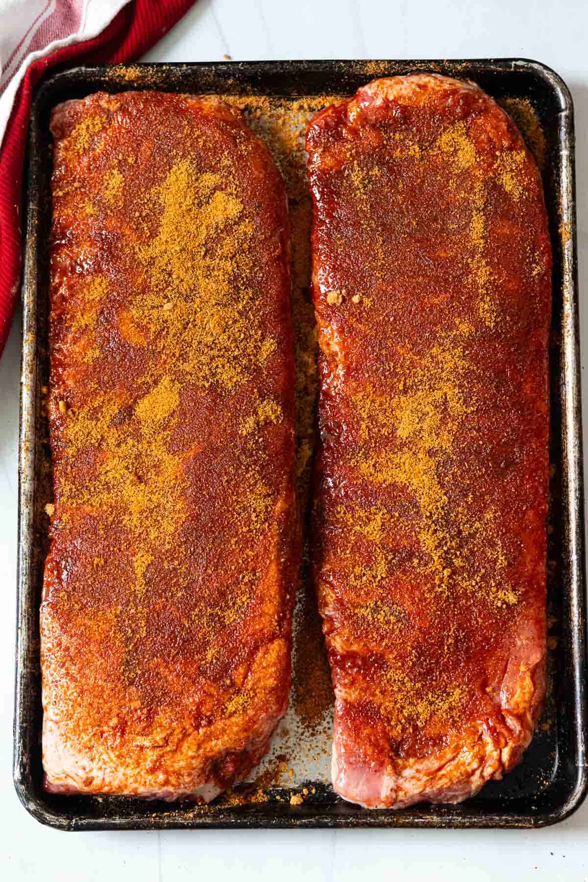 Two racks of ribs on a sheet pan with fajita brown sugar rub.