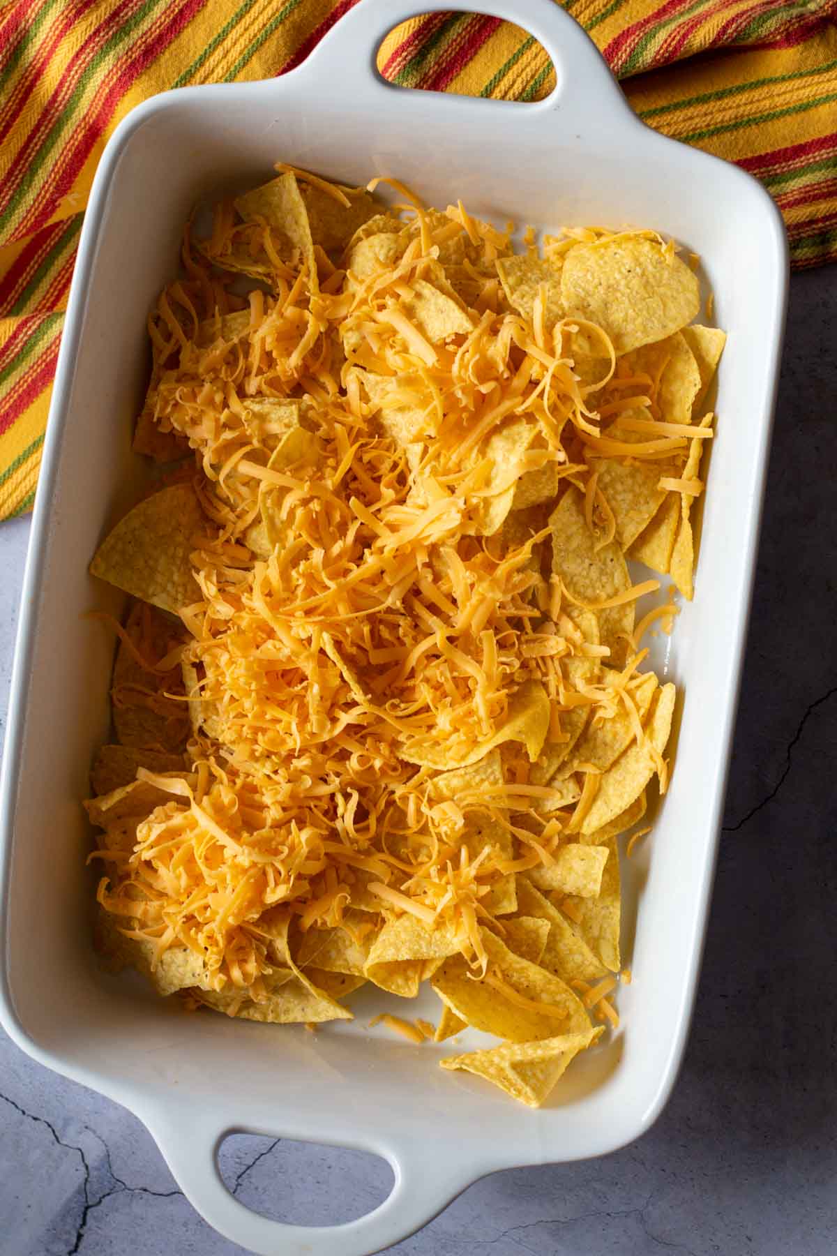 Adding cheese to corn chips in a casserole dish.
