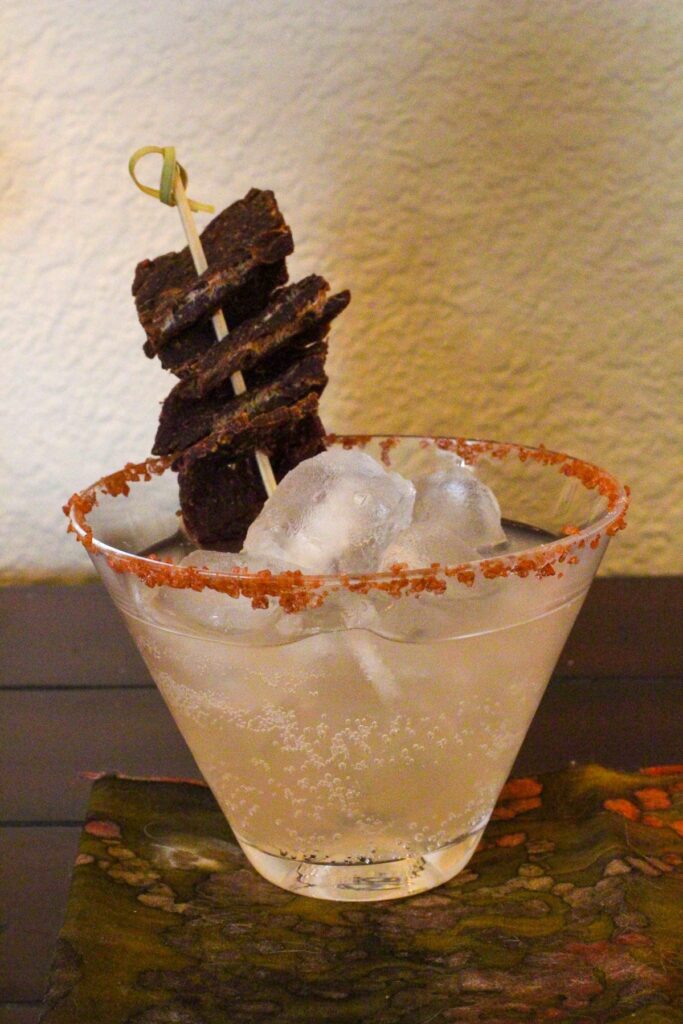 Cocktail glass with salty dog cocktail garnished with pink sea salt and beef jerkey