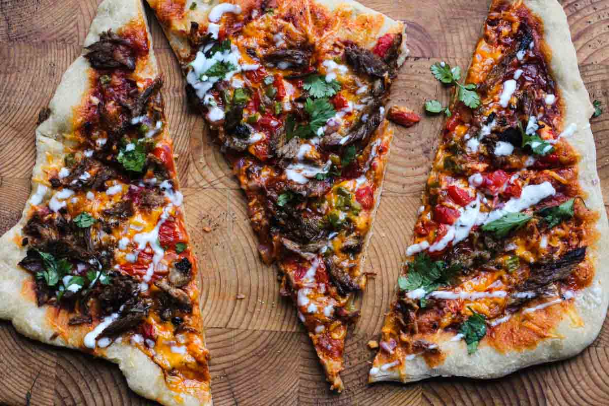 Slices of bbq brisket pizza with jalapenos and drizzled with ranch dressing.