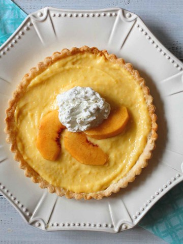 Peach curd tart topped with peaches and whipped cream.