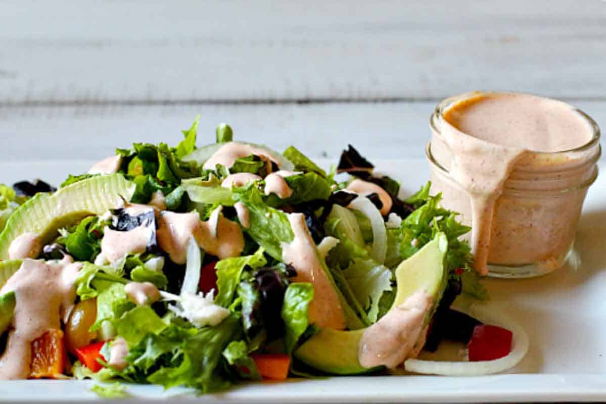 A jar of homemade spicy ranch dressing next to a dressed tossed salad.