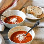 Two bowls of spicy tomato soup served with bread.