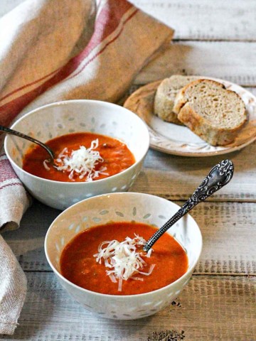 Two bowls of spicy tomato soup served with bread.