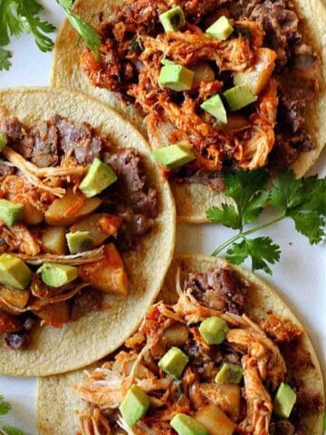 Tinga chicken tacos with toppings, served on a white platter.