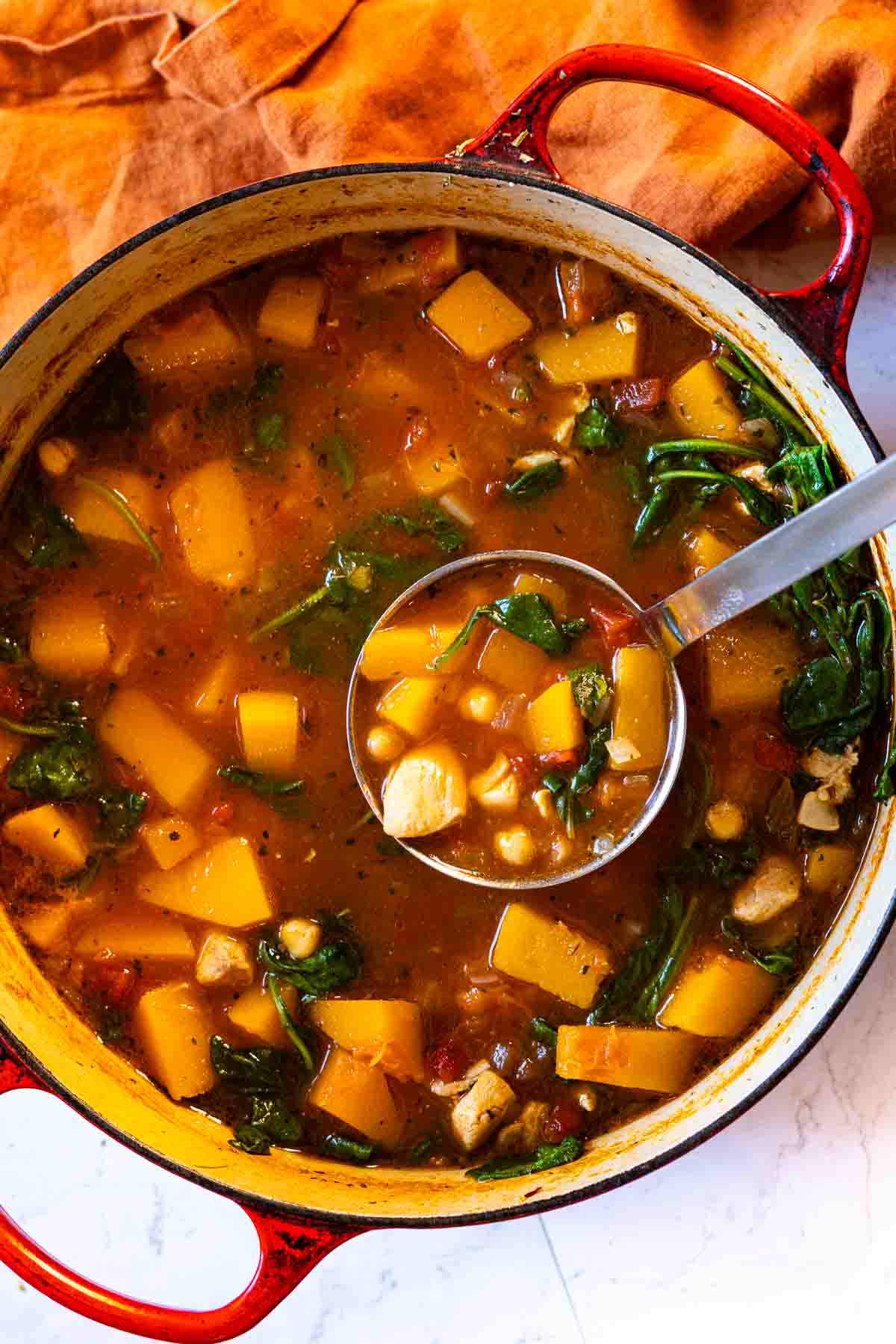 Butternut squash chicken soup in a le creuset Dutch Oven with a ladle of soup.