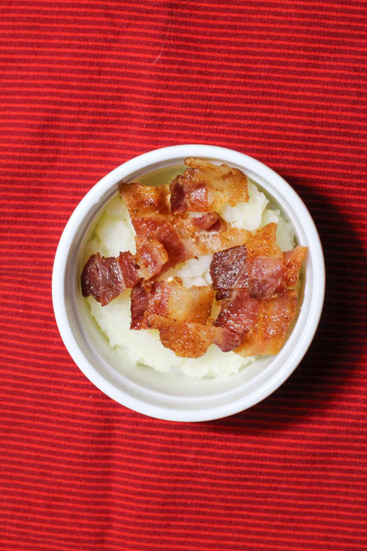 Mashed potatoes in a ramekin topped with crumbled bacon.