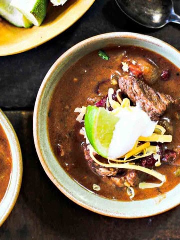 Bowls of chuck roast chili topped with sour cream and a wedge of lime.