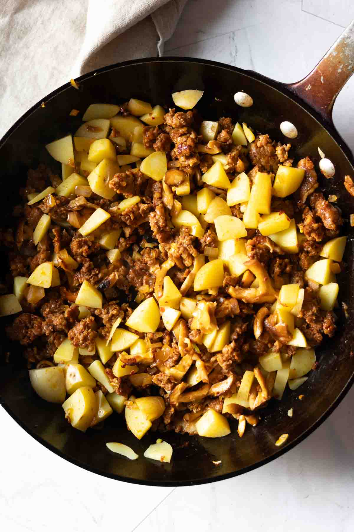 Adding potatoes to fried chorizo and mushrooms to make chorizo tacos.