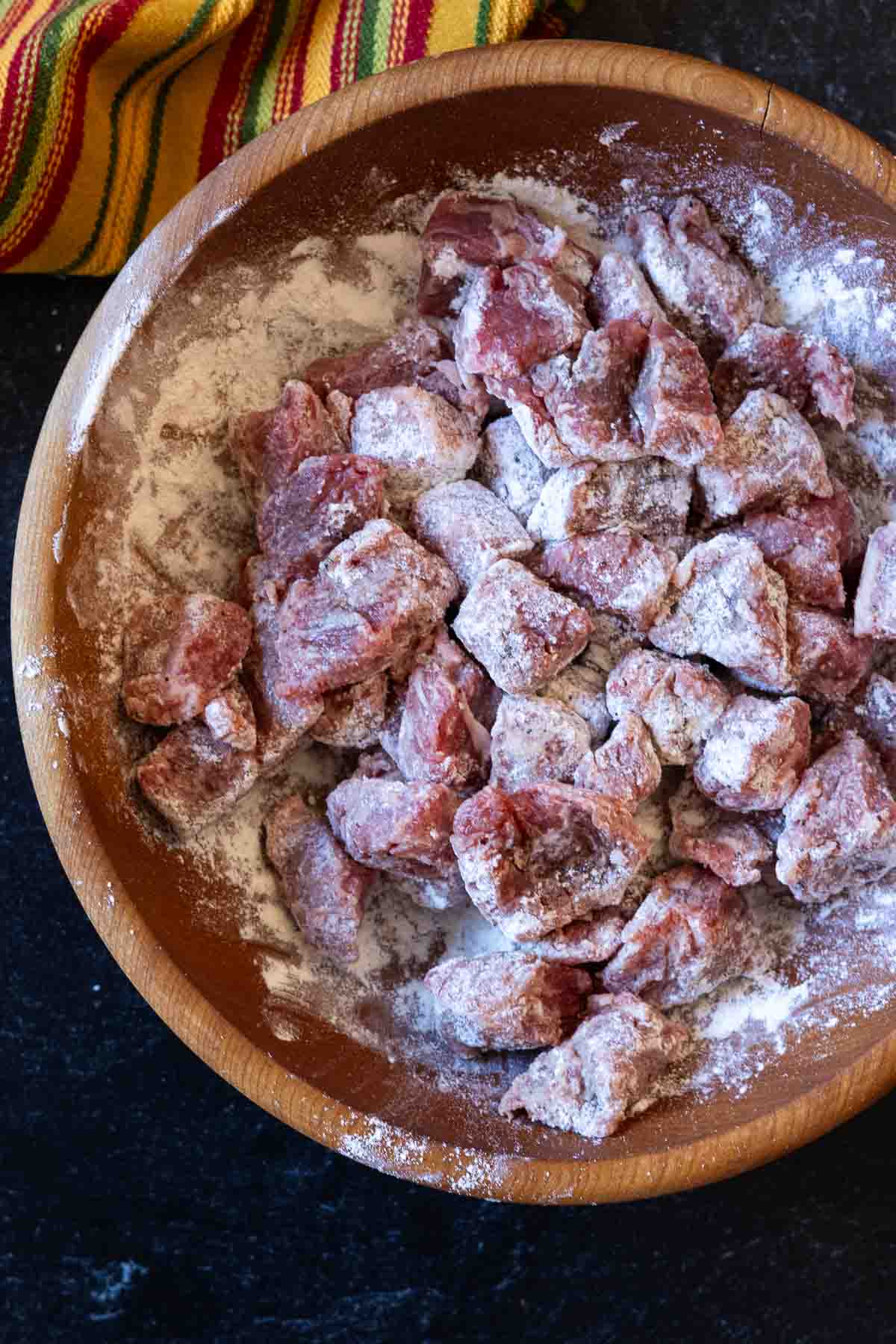 Coating stew meat with flour to make chuck roast chili.