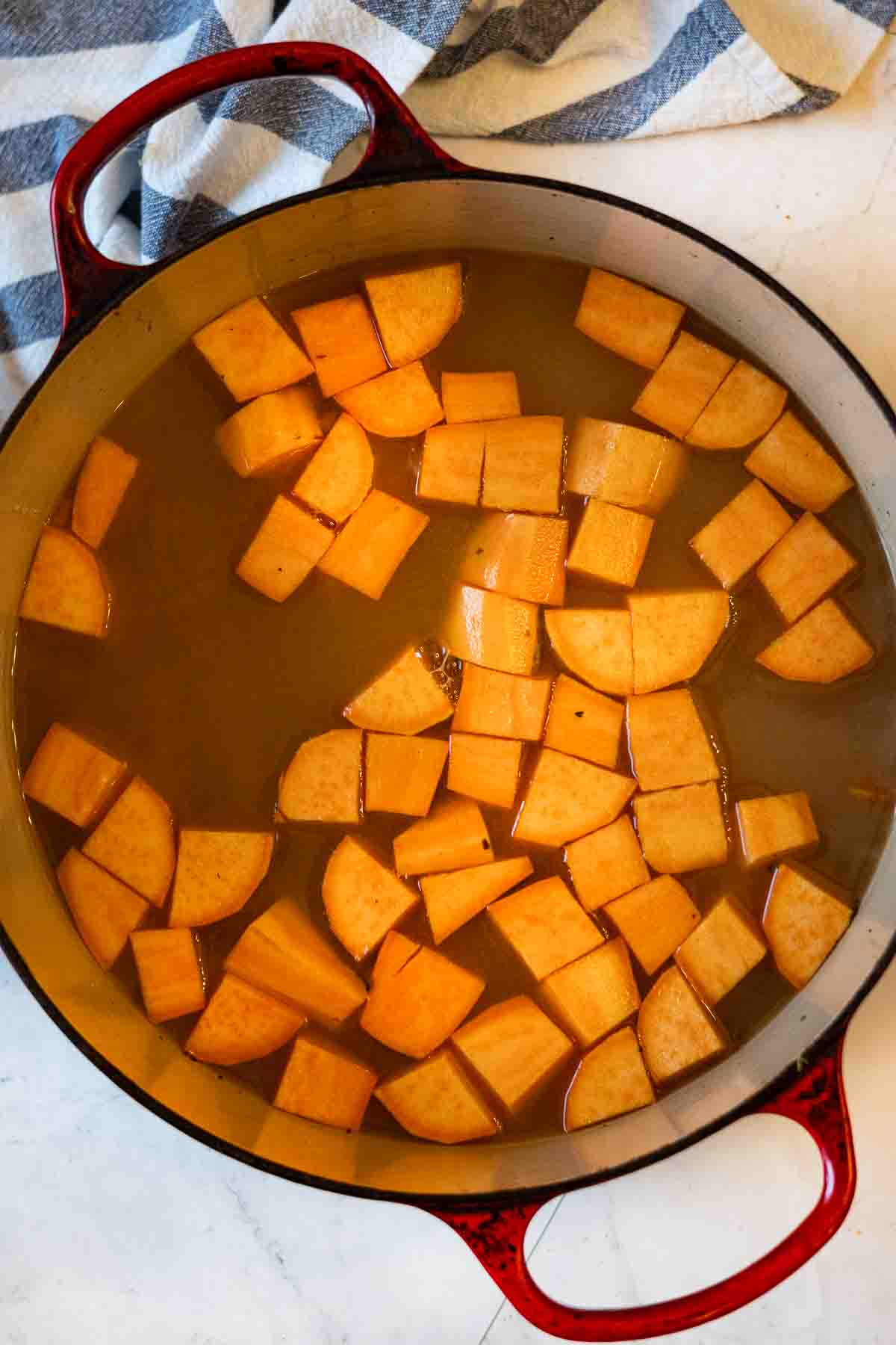 Adding sweet potatoes to white wine chicken broth to make chicken and vegetable soup.