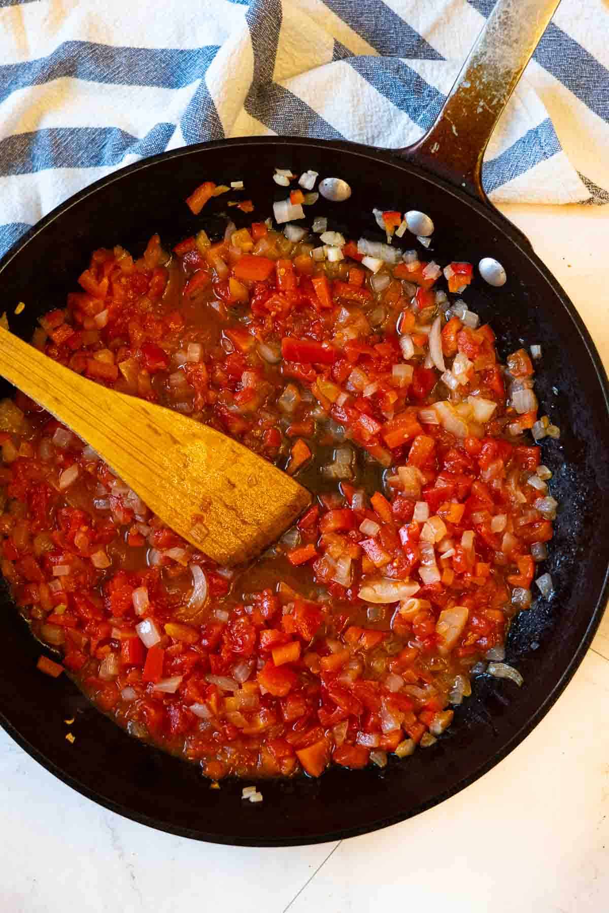 Adding tomatoes to sauteed vegetables to make chicken and vegetable soup with white wine.