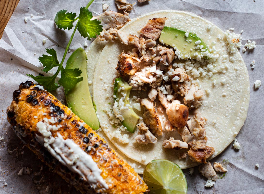 Grilled chicken thigh tacos on a corn tortilla served with grilled corn.