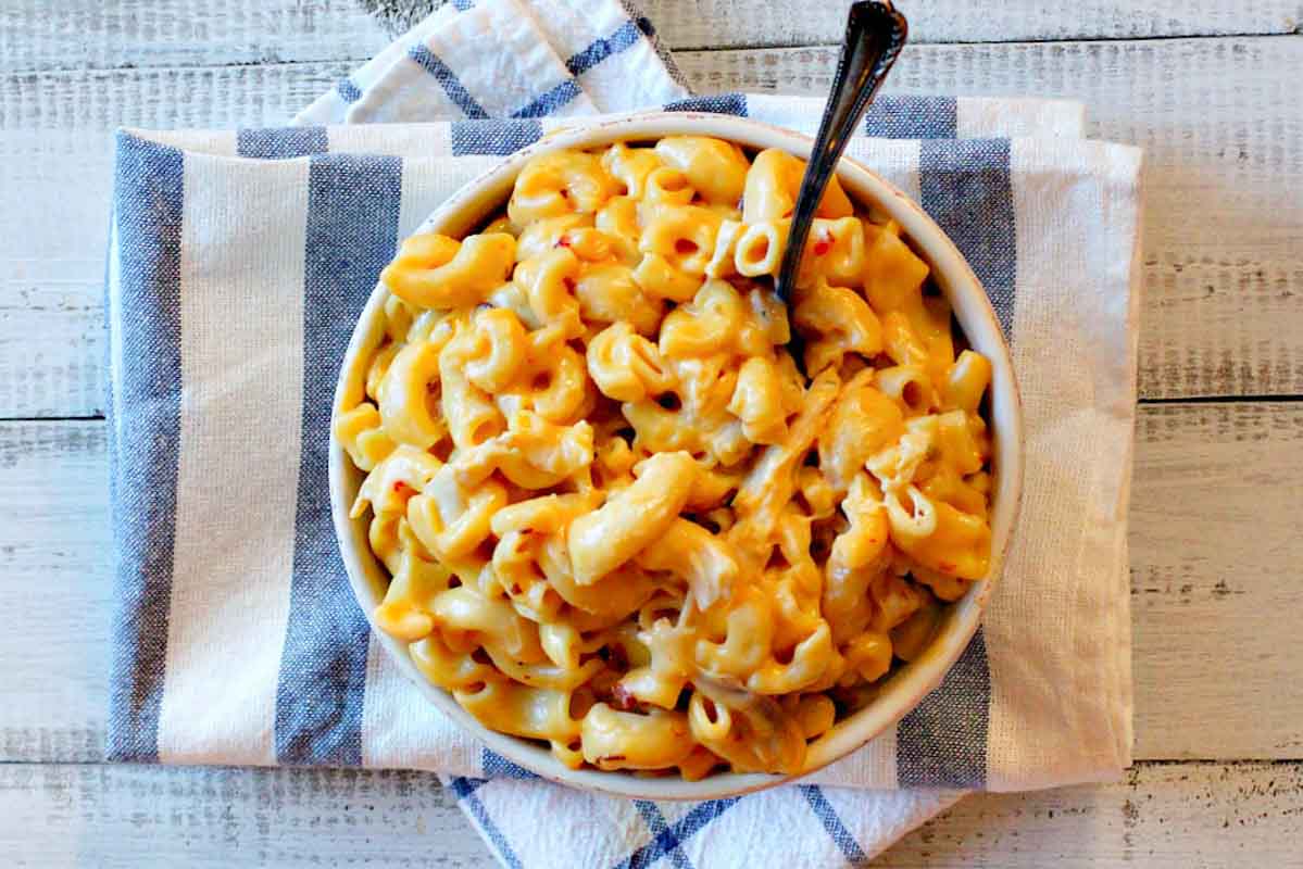 A bowl in mac and cheese with chicken on a blue striped towel.