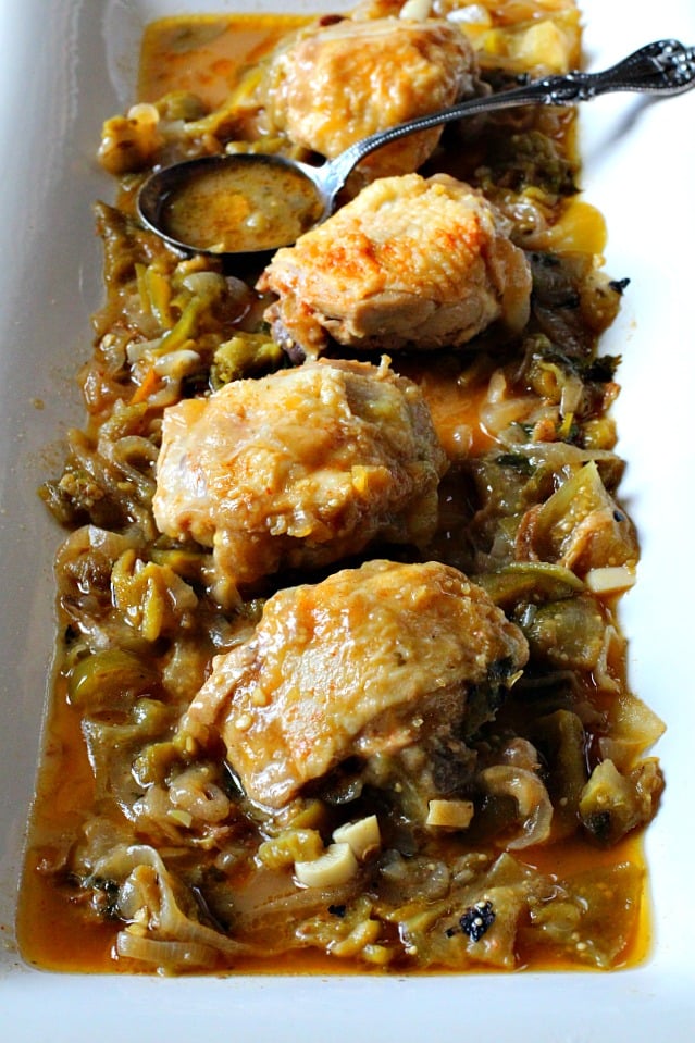 Crispy fried chicken thighs on a bed of tomatillo and hatch chile green sauce on a white serving platter