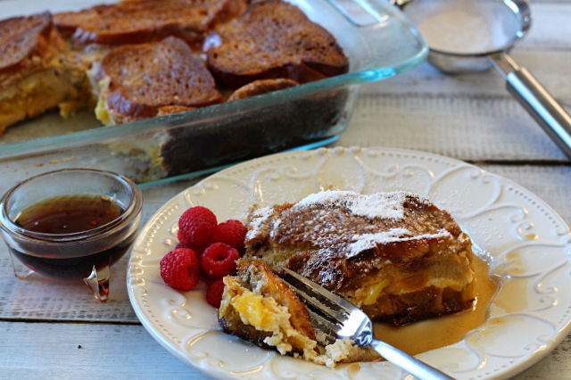A fork cutting a slice of mango cream cheese stuffed french toast with a side of fresh raspberries
