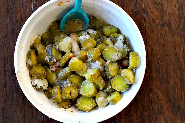 A bowl of sliced dill pickles mixed with sugar and red pepper flakes for homemade sweet spicy pickles.