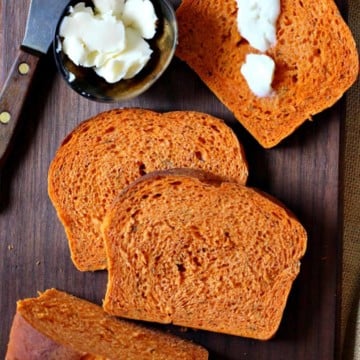 Italian Herbed Tomato Bread on a cutting board smeared with butter.