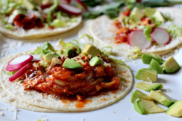 Chicken Soft tacos in a tomato sauce topped with chopped avocado and sliced radish.