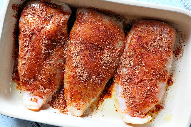 Boneless skinless chicken breasts coated with taco seasoning in a baking dish for Saucy Chicken Soft Tacos.