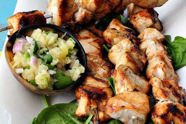 Grilled Chicken Kabobs on a white platter with fresh spinach and pineapple jalapeno salsa.