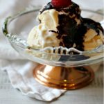 Mexican chocolate sauce over vanilla ice cream in a glass bowl topped with a raspberry.