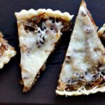 Caramelized Onion Tart with bacon and gruyere sliced and served on a wood cutting board.