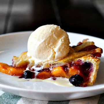 Peach and blueberry pie topped with a scoop of vanilla ice cream.