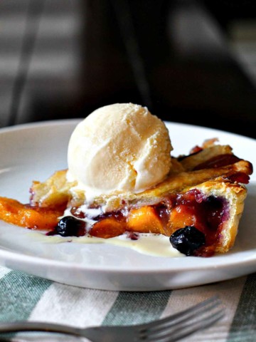 Peach and blueberry pie topped with a scoop of vanilla ice cream.
