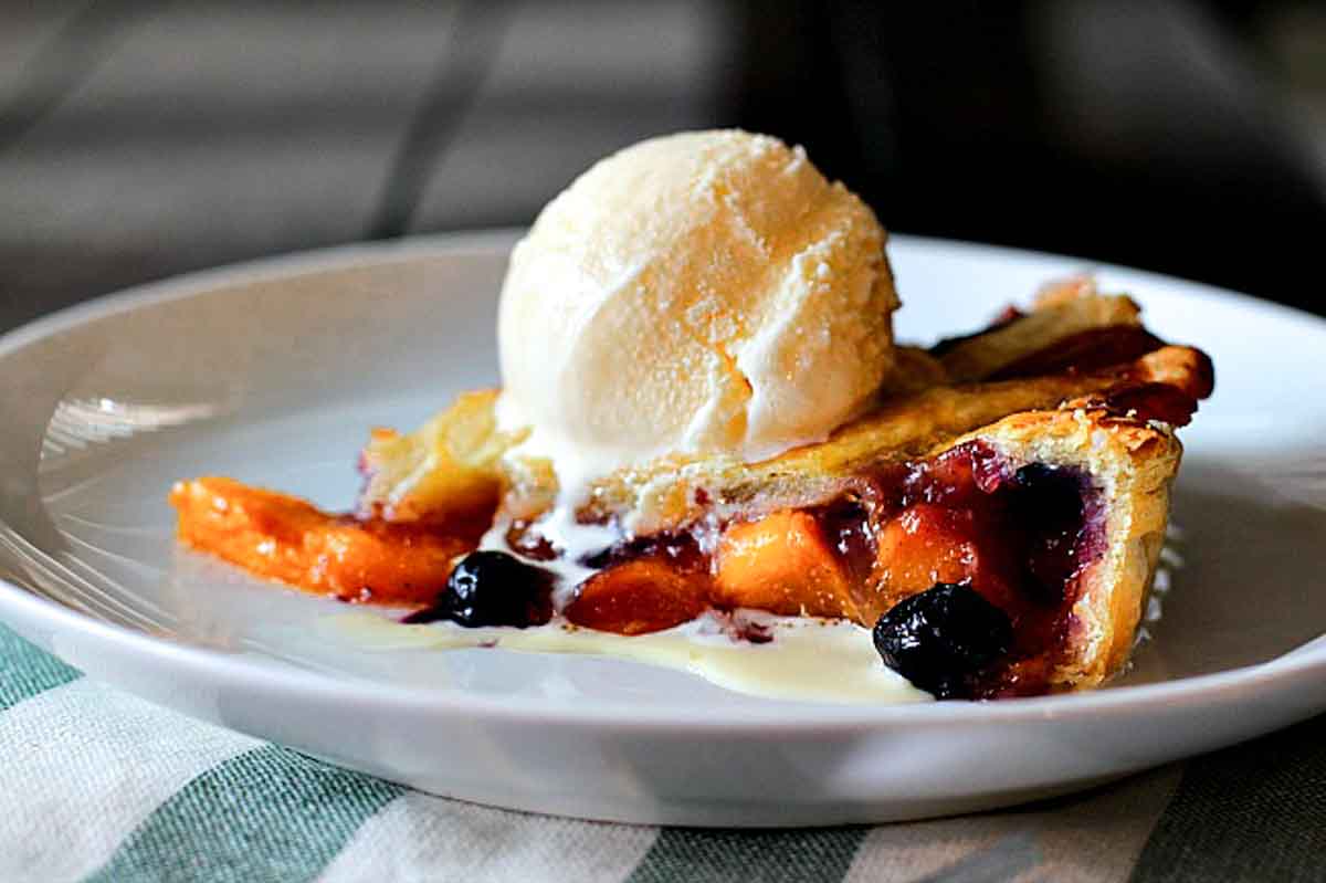 A slice of blueberry and peach tart topped with a scoop of vanilla ice cream.