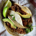 Shredded pork tacos with Achiote Sauce topped with slices of avocado.